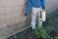 Man spraying the exterior of a building with a long, thin nozzle.