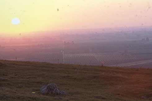 Orchards and a colorful sunset viewed from a hilltop through smoggy air.