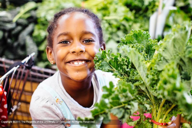 Young child holding a bunch of leafy greens.